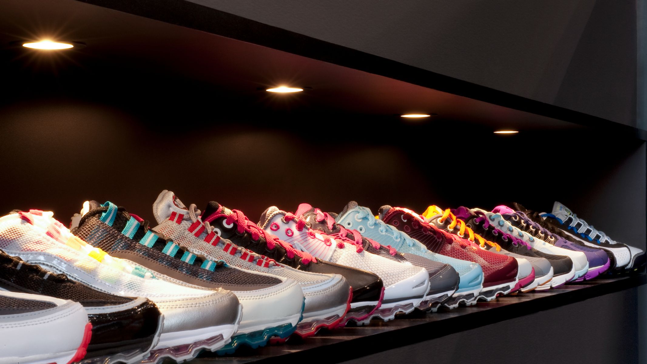 A variety of running shoes are displayed in a shop under warm downlights 
