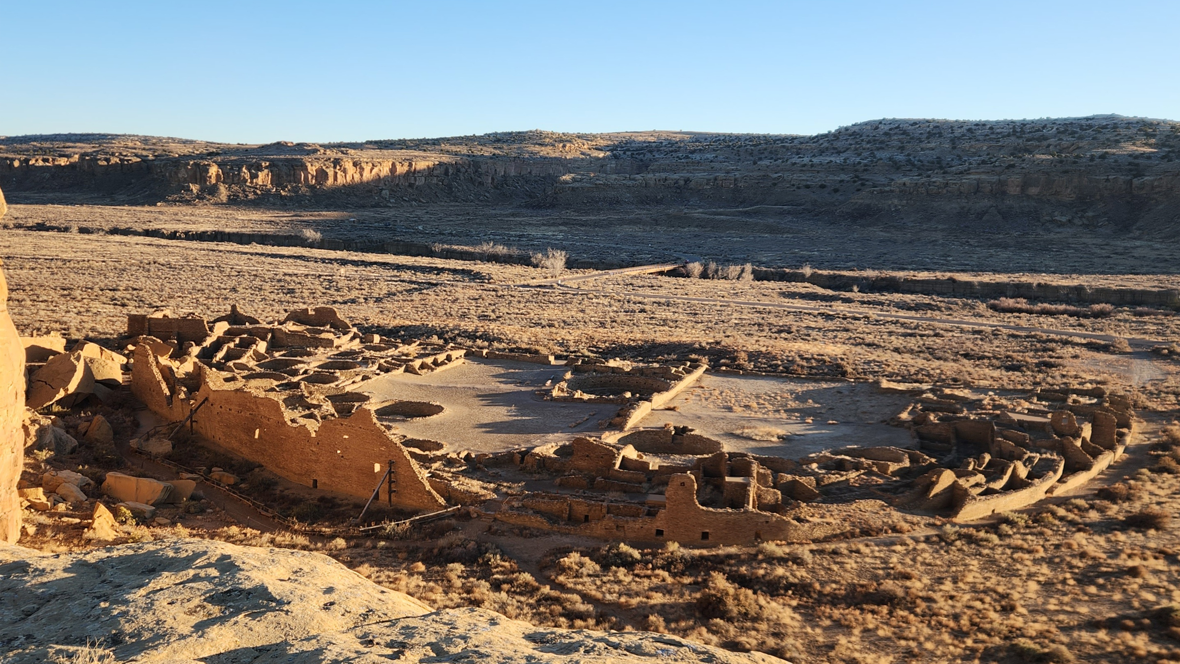 Ruins of a large circular building on a plant plain with mountains in the background.